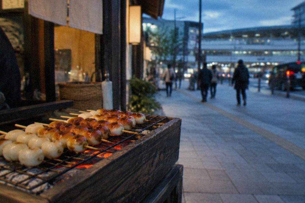 Skewered rice cakes grilling over charcoal on a small shop counter