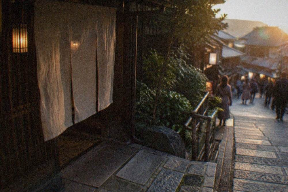A traditional Kyoto restaurant entrance with a wooden noren curtain and stone path at dusk