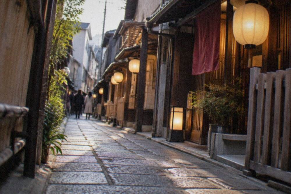 A narrow stone-paved alley at dusk with glowing lanterns hanging outside wooden restaurant fronts