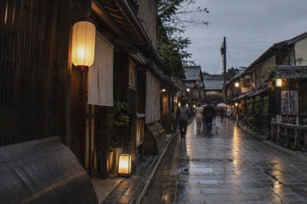A quiet lantern-lit street in Gion with traditional wooden machiya facades in the evening