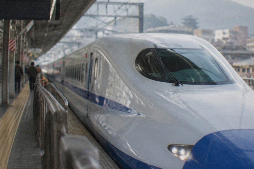 A blue-and-white Shinkansen bullet train waiting on a platform at a Japanese railway station