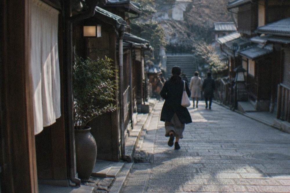 A narrow preserved Kyoto street of wooden machiya shopfronts sloping downhill toward a stone stairway in soft evening light
