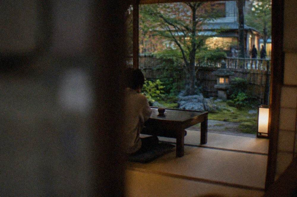 An open tatami room in a ryokan facing a small moss and stone garden at dusk