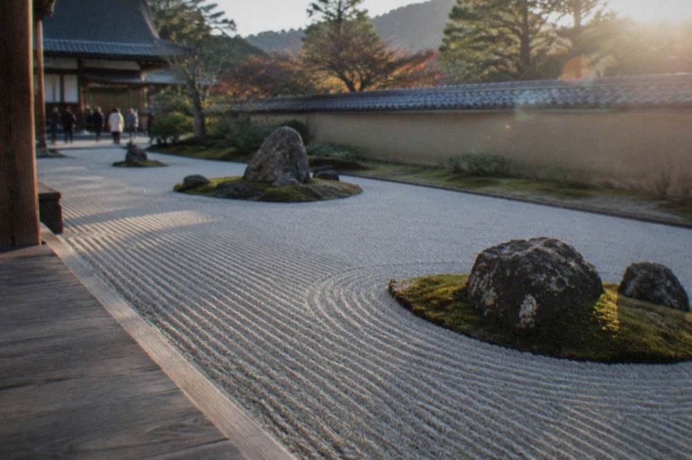 A raked gravel rock garden at a Kyoto Zen temple, with moss and a tiled temple wall behind it