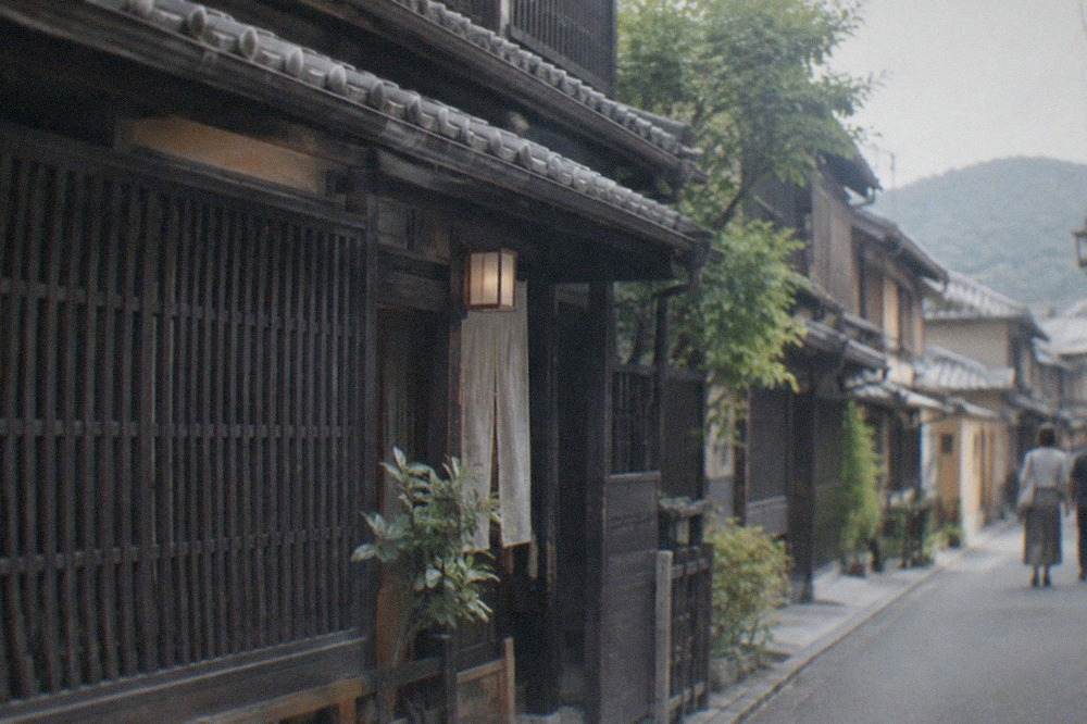 A narrow wooden Kyoto machiya townhouse with dark lattice facade and tiled roof seen from the street