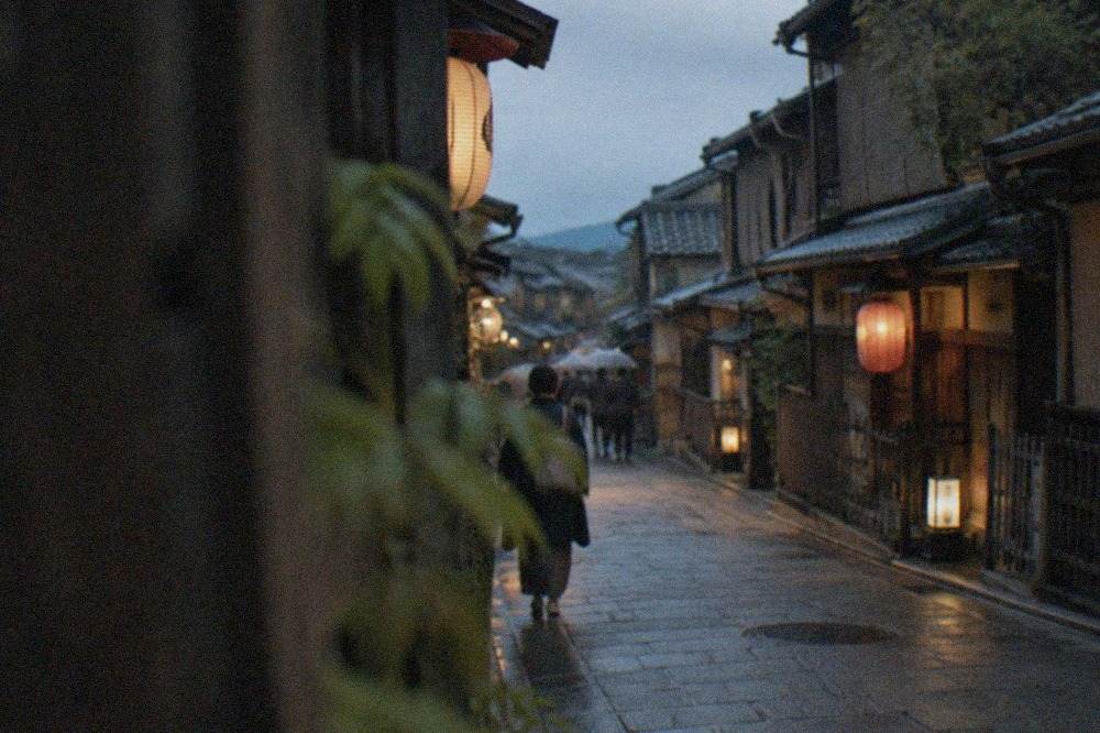 A lantern-lit traditional wooden street in Kyoto at dusk with machiya facades