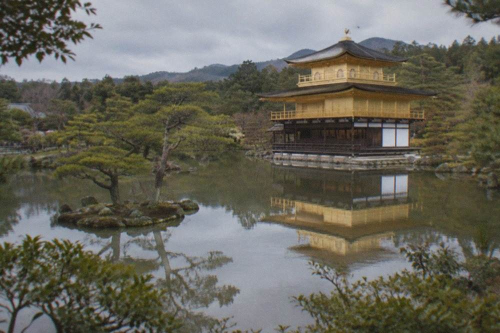 A golden temple pavilion reflected in a still pond surrounded by pine trees