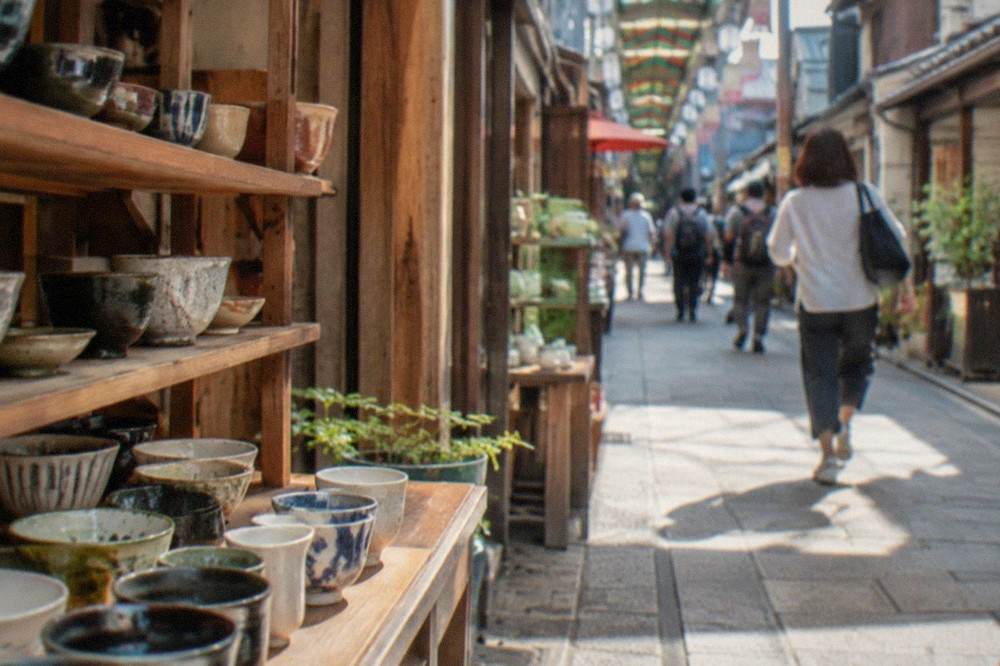 Ceramic bowls and cups displayed on wooden shelves in a small Kyoto pottery shop