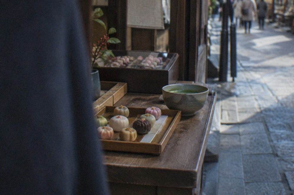 A tray of small Japanese sweets arranged on a wooden counter beside a bowl of whipped matcha