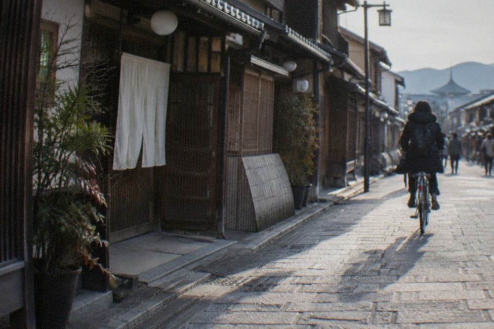 A quiet stone lane in Kyoto with traditional wooden machiya facades and a cyclist passing through