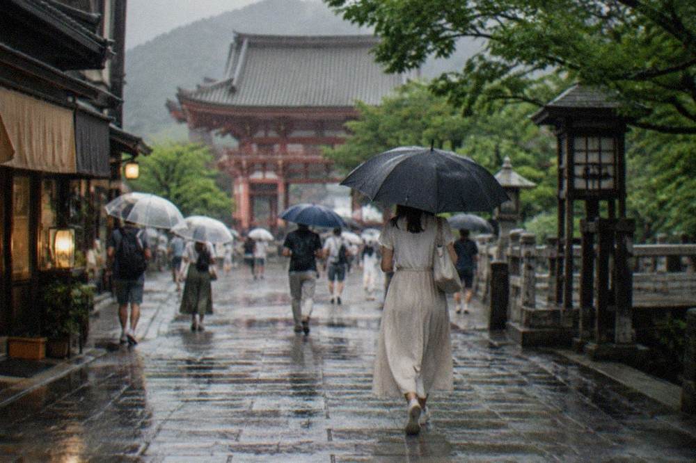 Visitors with umbrellas crossing a temple approach in heavy summer rain in Kyoto