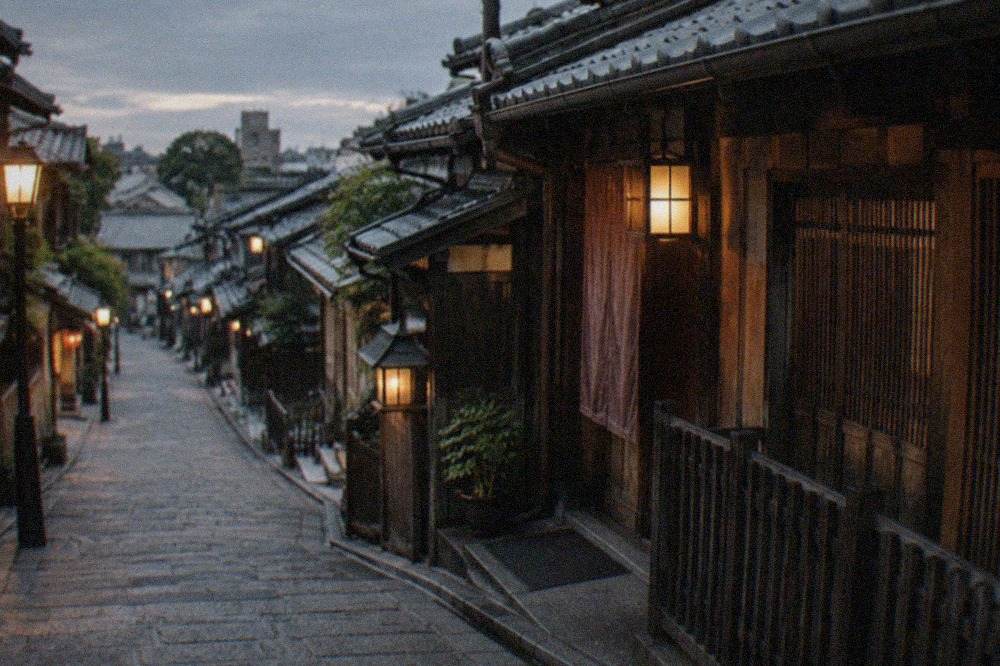 A narrow stone-paved alley in Kyoto's Gion district at dusk, with traditional wooden machiya facades and lanterns, and no people in the frame