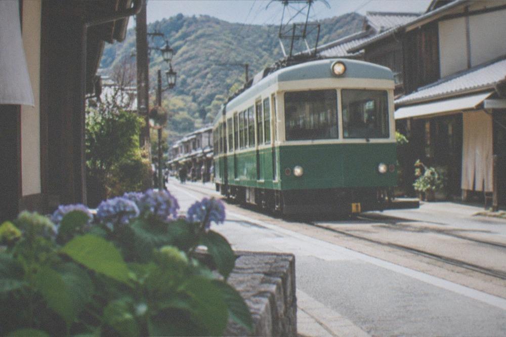 A single-car tram moving along a street-level track past small houses and shops