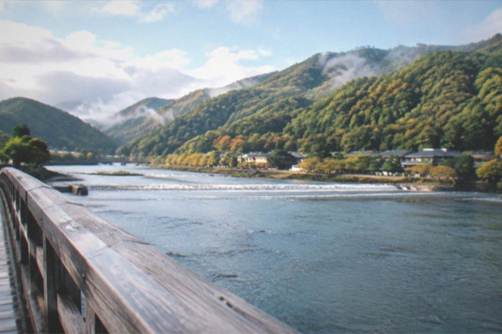 A wide river view from a wooden bridge with forested mountains rising behind the water in morning light