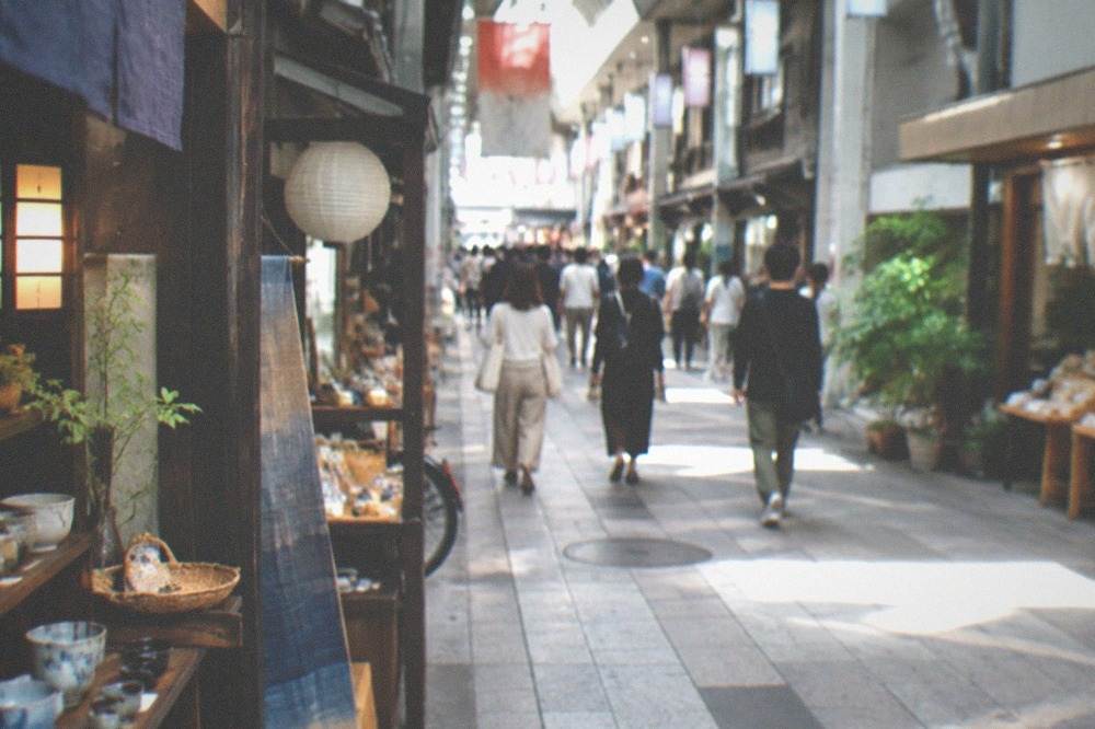 A covered arcade street in Kyoto with hanging lanterns, small specialty shops and pedestrians browsing