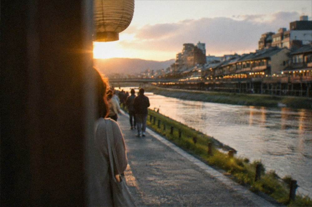A riverside walking path in Kyoto at dusk with lit restaurant terraces along the far bank