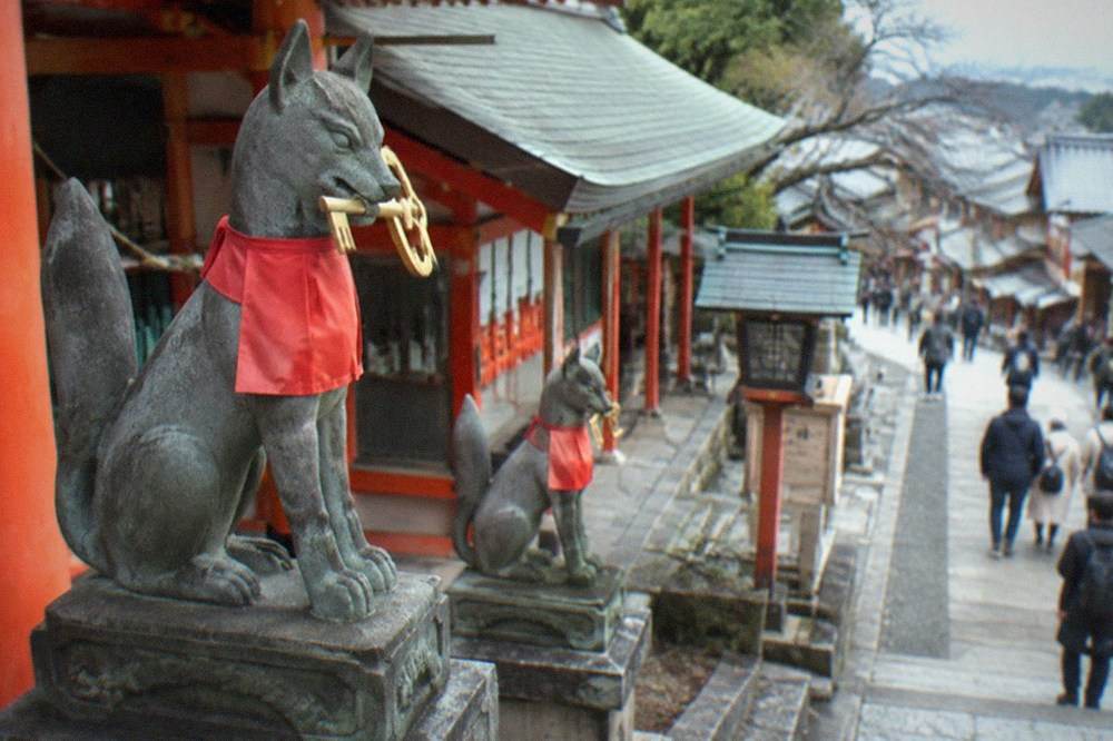 Fox statues holding keys in front of a shrine building at Fushimi Inari