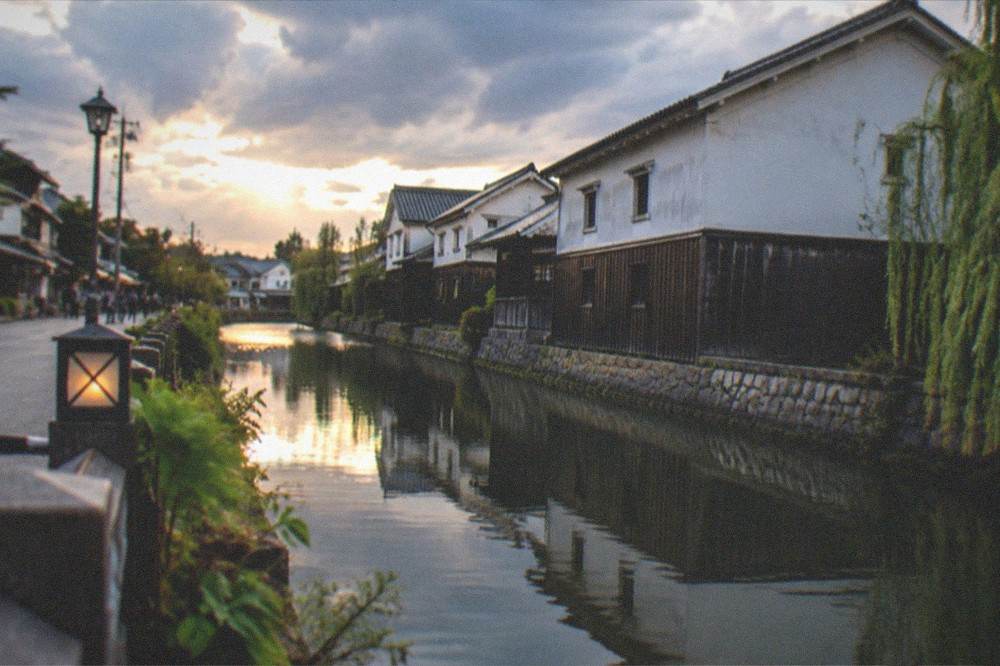 Evening light on a canal in the Fushimi sake district with brewery warehouses reflected in the water