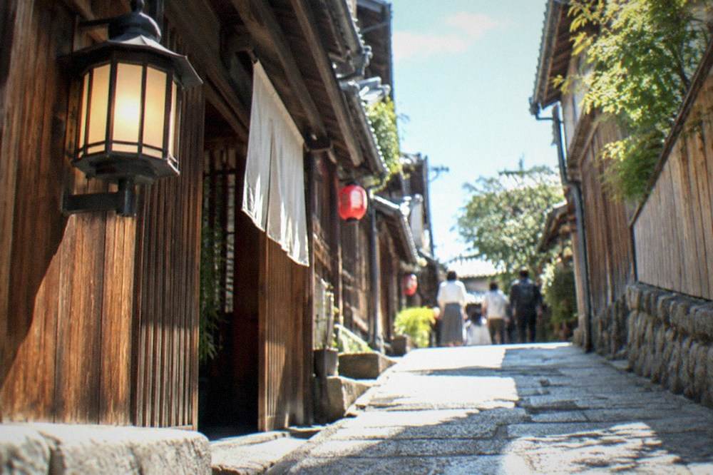 A narrow stone-paved alley with wooden doors and a lantern in Gion