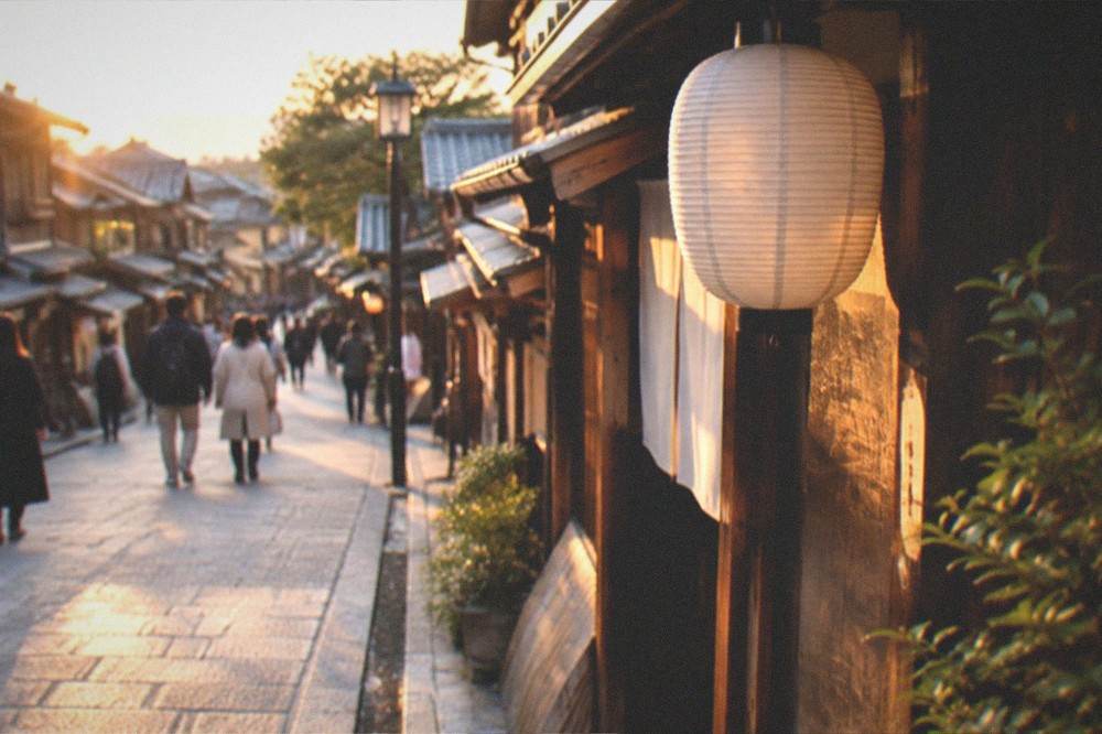 A maiko in an elaborate kimono walking along a lantern-lit Gion street in the evening