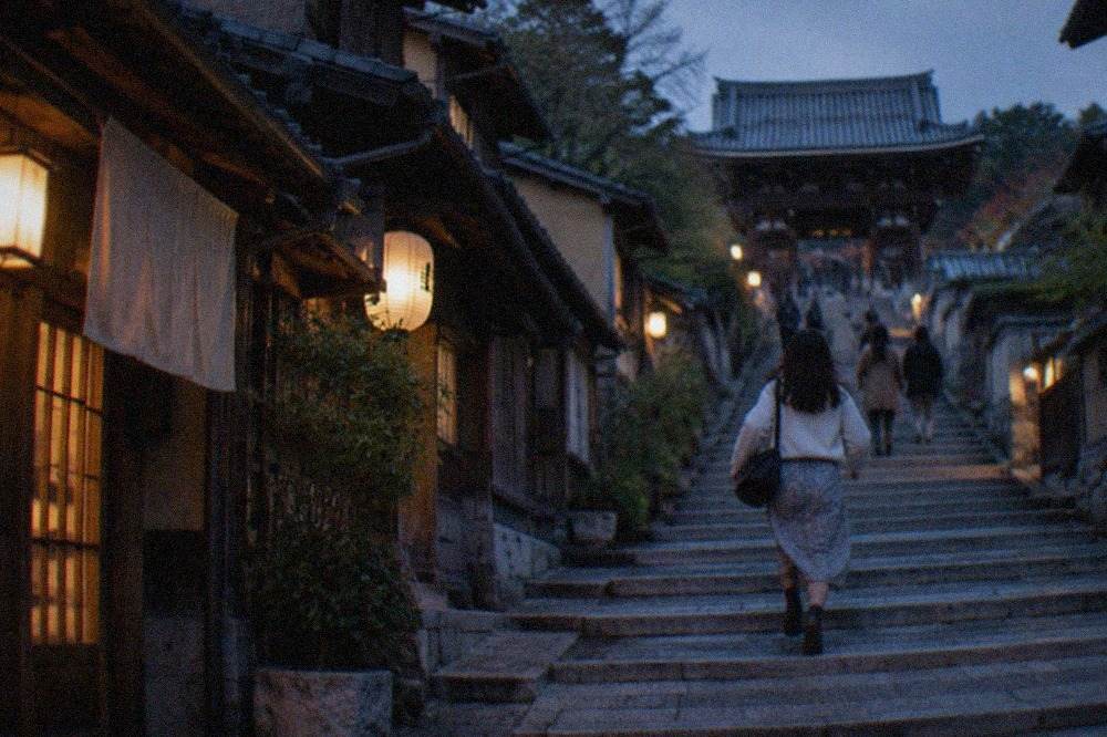 Stone steps of a preserved old Kyoto street lined with traditional machiya shopfronts rising toward a temple gate