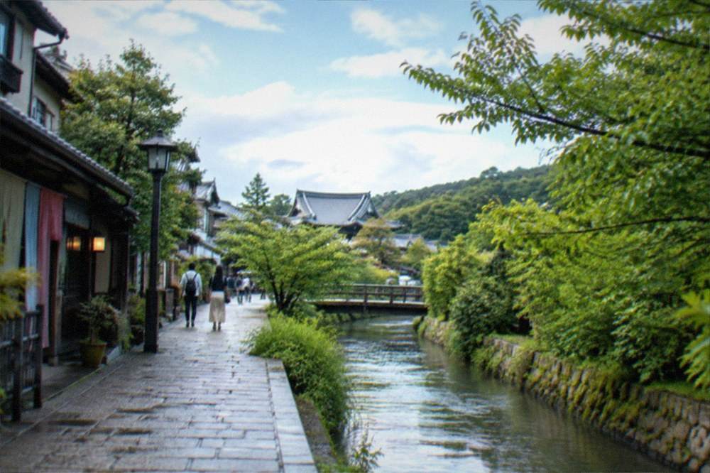 Stone path along a narrow canal lined with trees leading toward temple rooftops