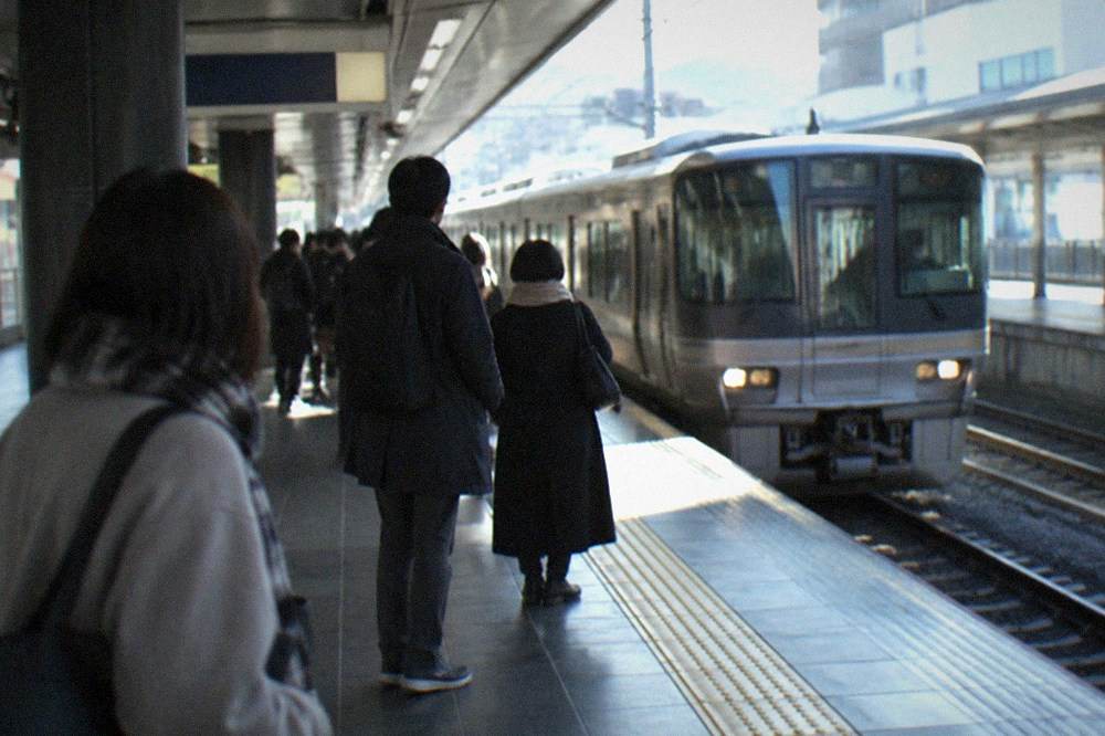 A subway platform in Kyoto with a train arriving and passengers waiting behind the yellow line