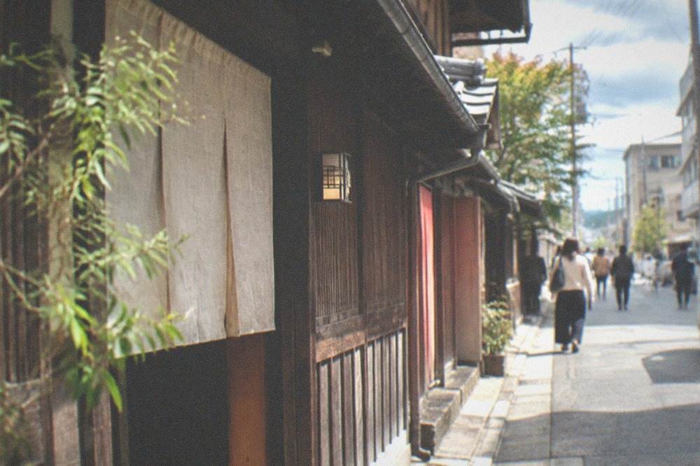 A green Kyoto city bus stopped at a street corner in a residential neighbourhood