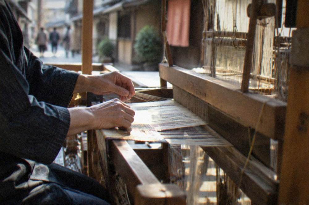 A craftsman's hands working silk threads on a wooden loom