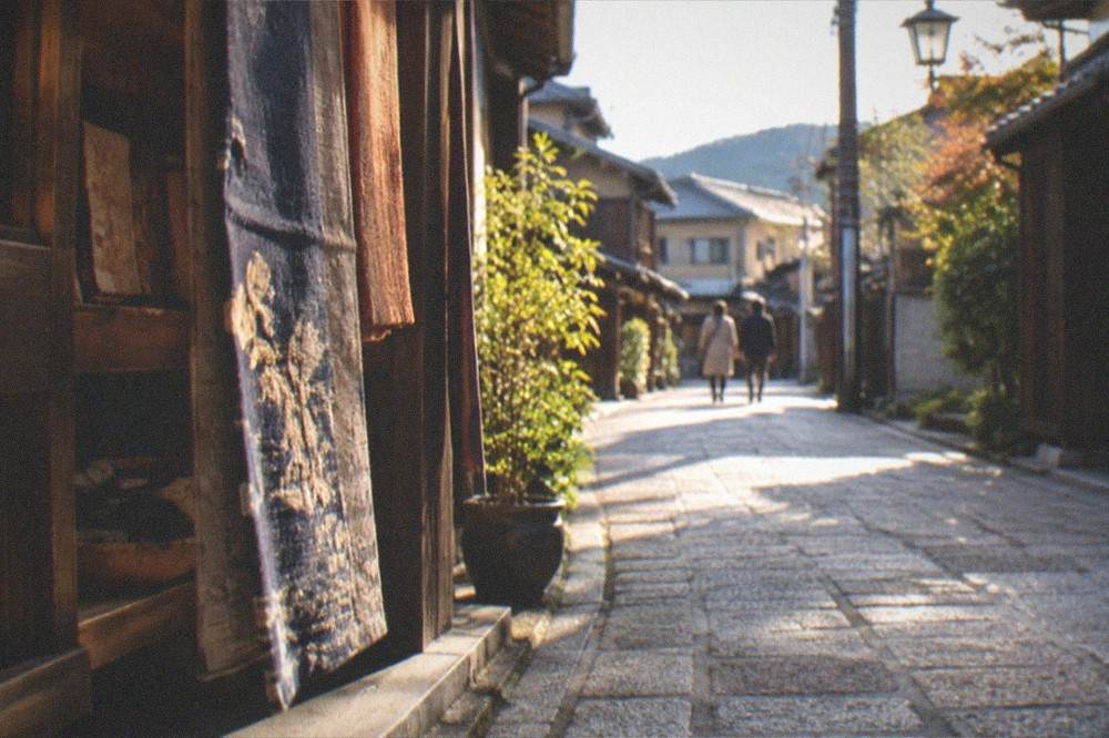 Late afternoon light on a stone-paved lane between wooden workshop buildings