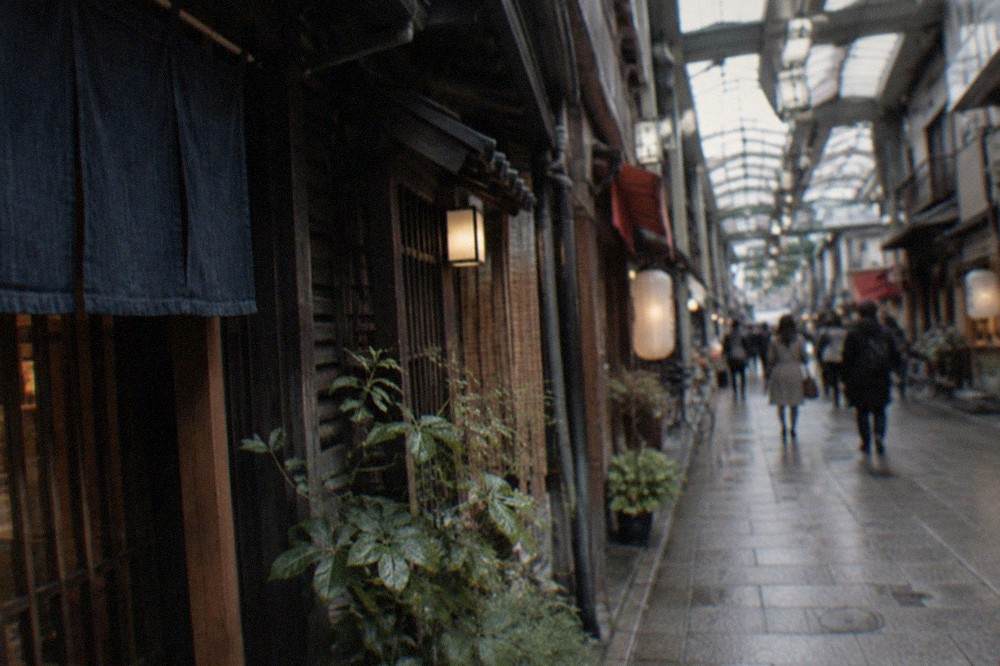 A narrow covered arcade lane in Kyoto with traditional shop signs and a few pedestrians