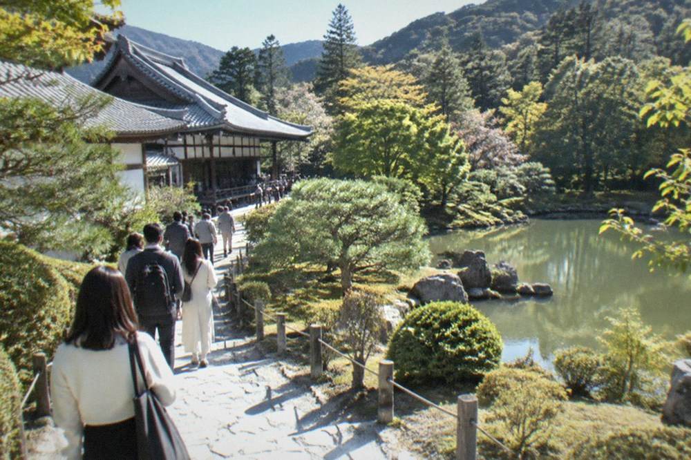 Visitors walking a stone path beside the garden grounds of Tenryu-ji temple in Arashiyama