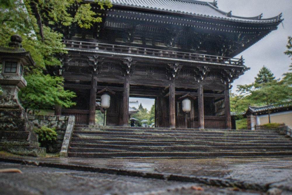 A massive two-storey wooden temple gate rising above stone steps with a large roof and lanterns