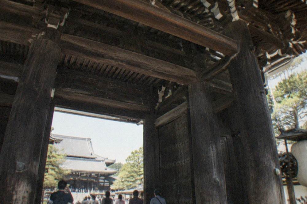 Visitors standing small beneath the towering wooden beams of a temple gate looking up