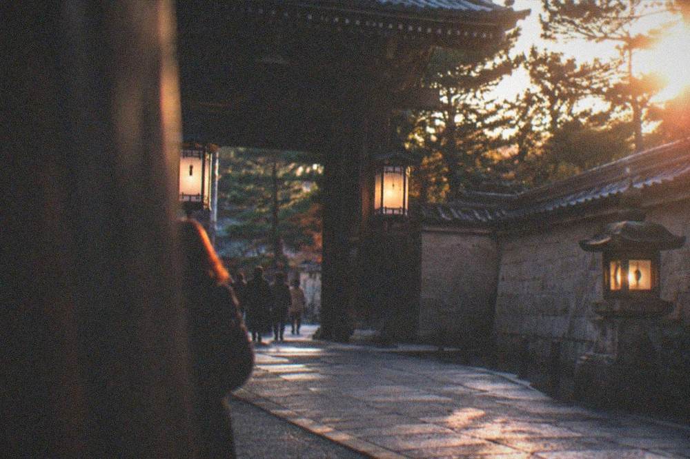 A lantern-lit stone gate and wall in the evening in a historic temple district