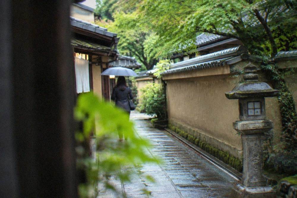 A quiet lane between earthen temple walls with tiled roofs and a single stone lantern