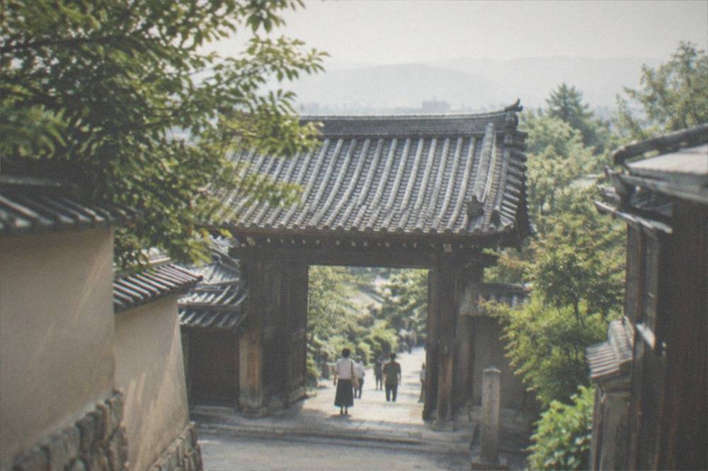 A wooden temple gate with heavy tiled roof seen from a narrow lane between walls