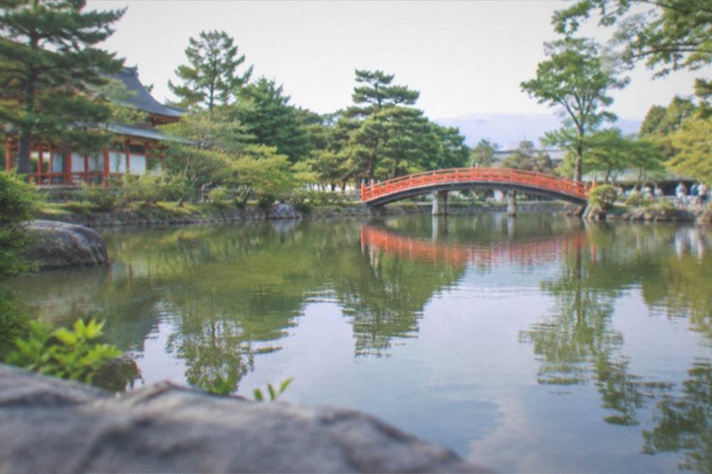 The garden pond at Heian Shrine reflecting trees and a red bridge