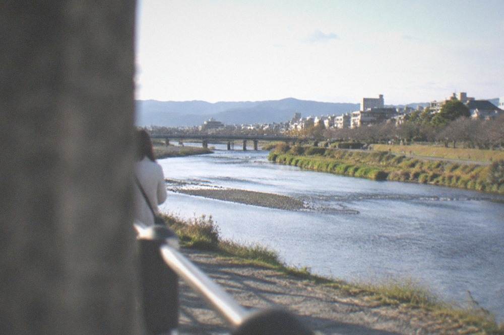 A wide gravel river channel running between green banks and city rooftops