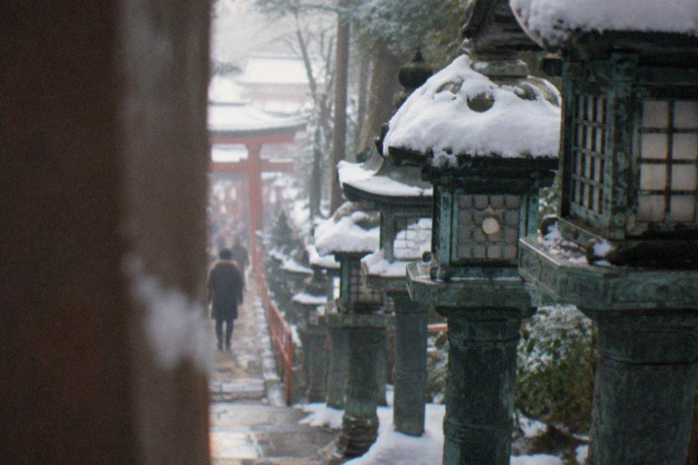 Close view of weathered green iron lanterns standing in a row along the shrine steps, each capped with snow