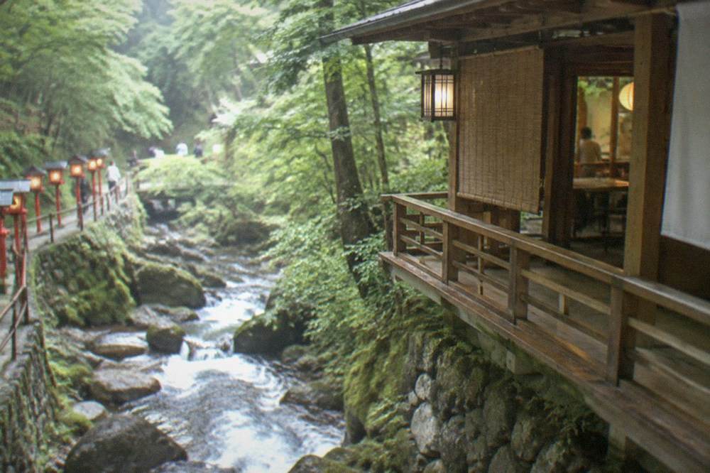 A fast mountain stream running over stones beside a wooden shrine building in a cedar valley