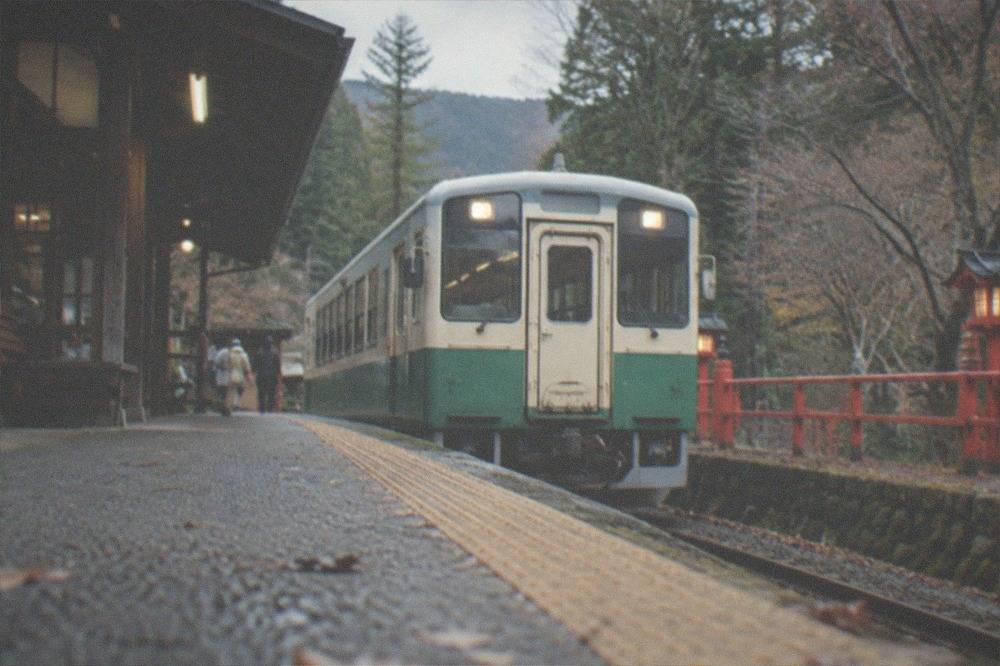 A small single-car local train waiting at a rural mountain station surrounded by trees