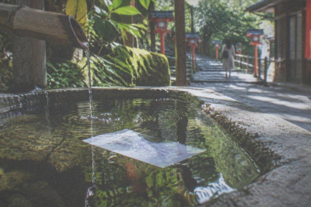 A white paper fortune floating on the surface of a shallow stone basin, characters appearing through the wet paper