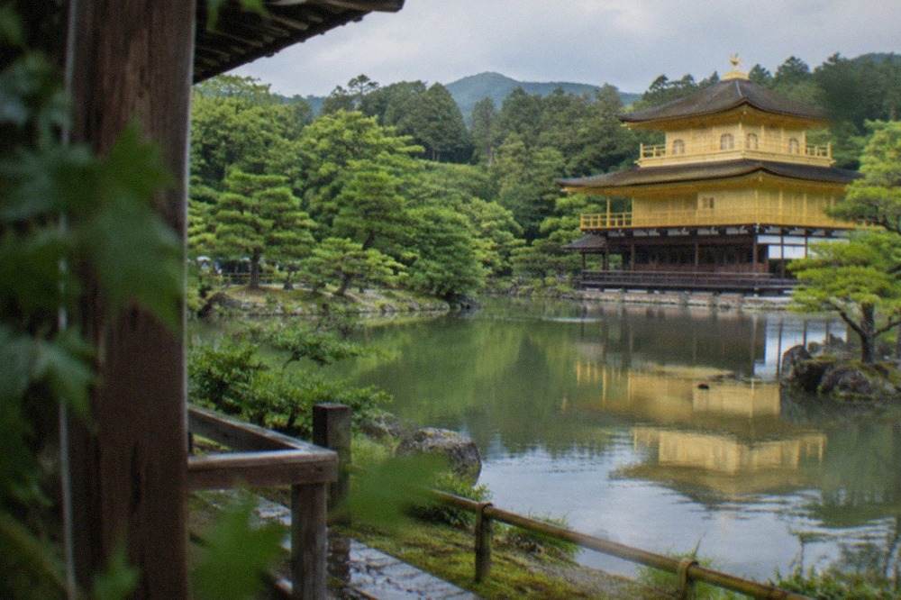 The golden pavilion of Kinkaku-ji reflected in the pond in front of it, with pine trees on the far bank