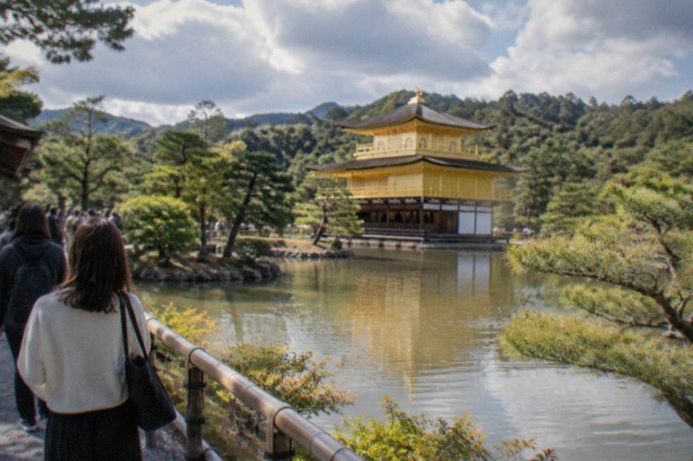 Visitors walking the garden path beside the pond at the Golden Pavilion on a bright morning