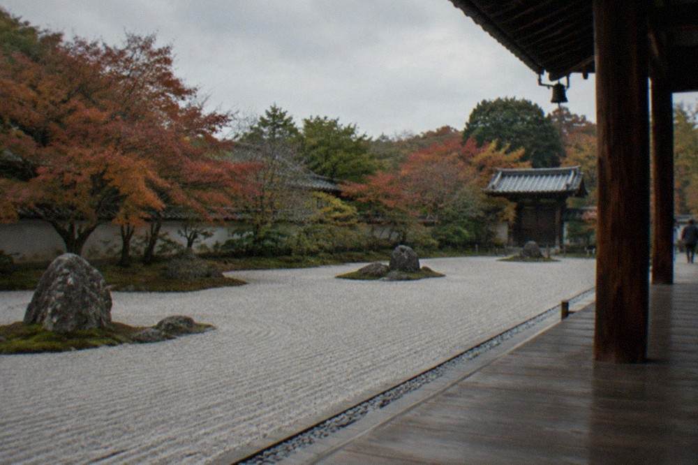 Raked gravel and clipped maple trees in a Kyoto Zen temple garden seen from a wooden veranda