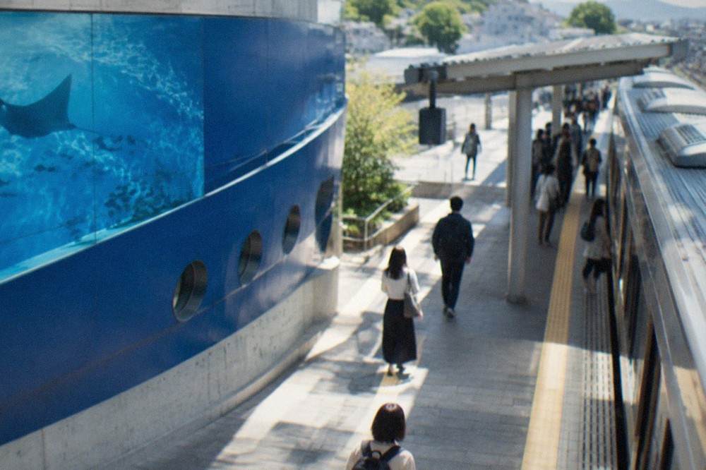 A clean modern train platform with a signboard and a few travellers waiting