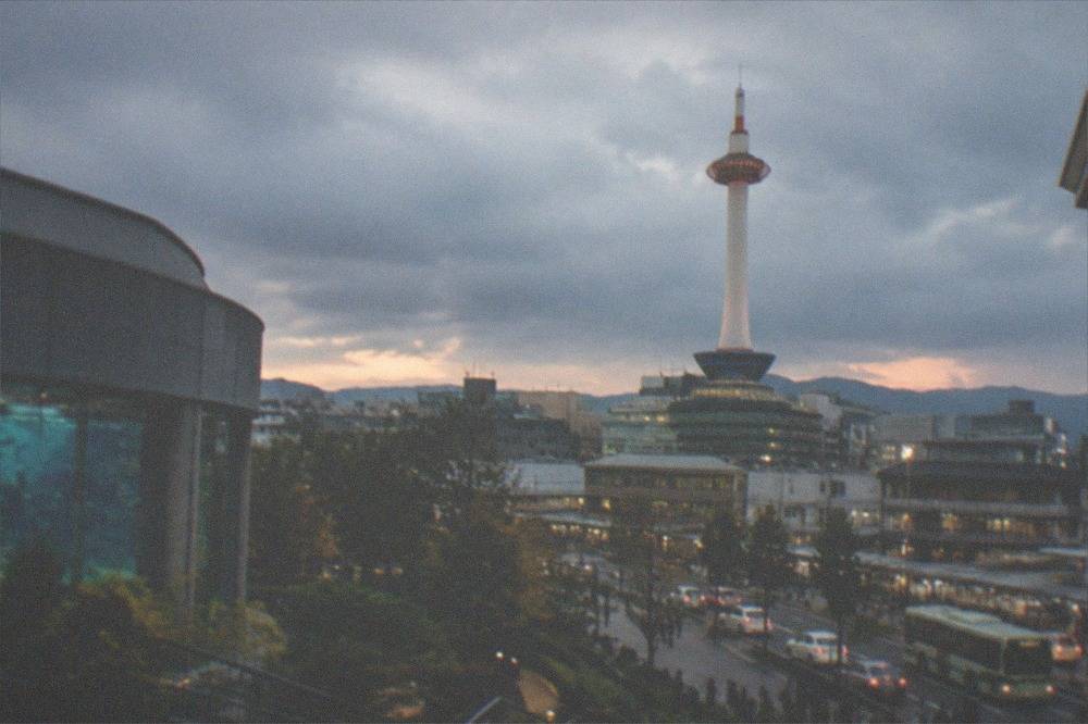 A tall white observation tower rising above city rooftops at dusk