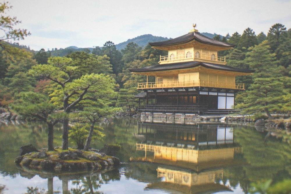 A golden pavilion reflected in a still pond surrounded by trees at Kinkaku-ji temple in Kyoto