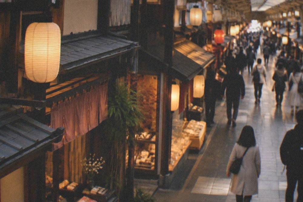 A covered shopping arcade street with lanterns and small shops lit in the evening in downtown Kyoto
